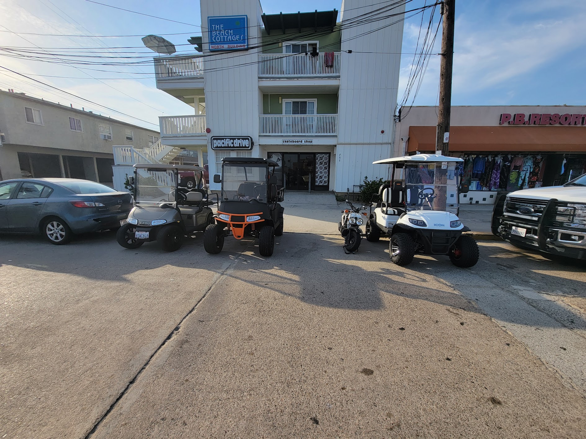 Several golf carts parked together in front of Pacific Beach shops.
