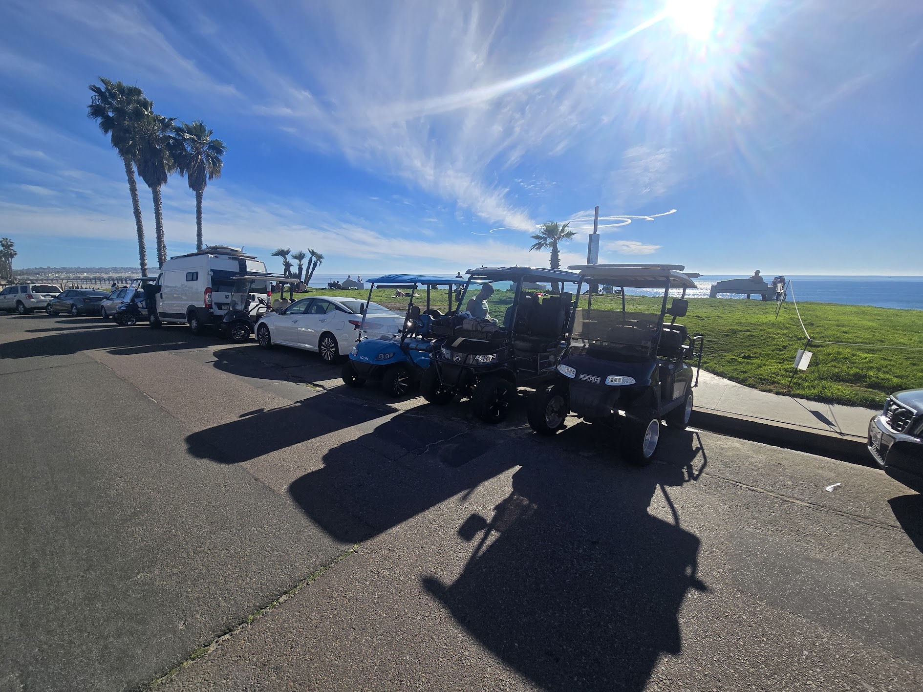 Golf carts parked along the coast beside standard vehicles.